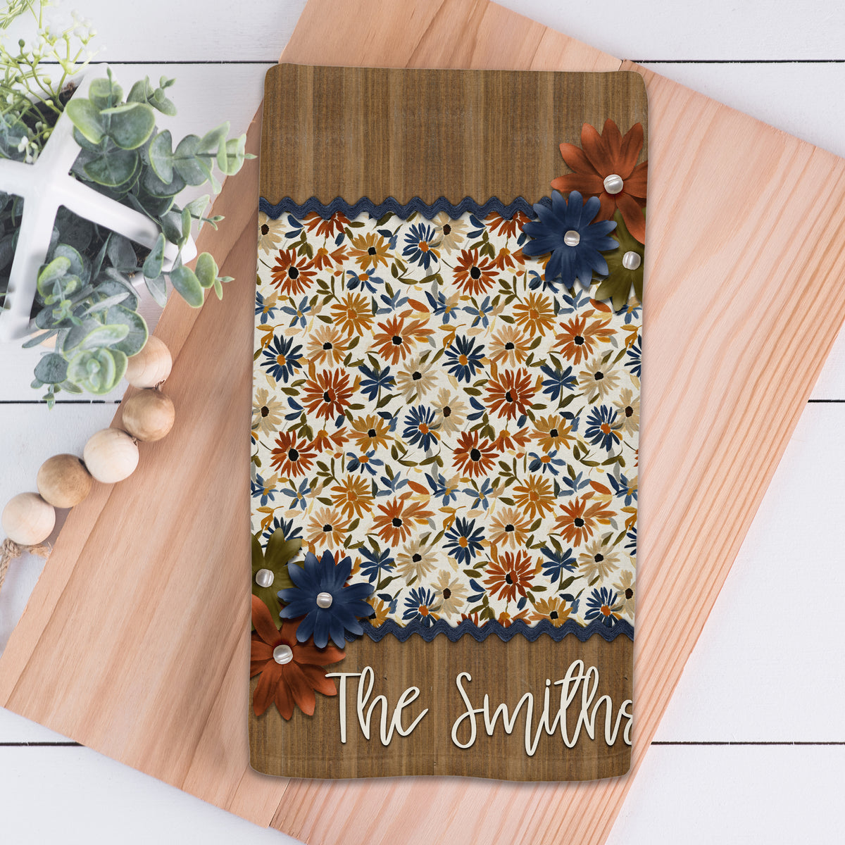 Personalized fall kitchen towel featuring navy, rust, golden yellow, and olive floral patterns with layered flower accents, navy trim, and a rustic wood-look family name panel.