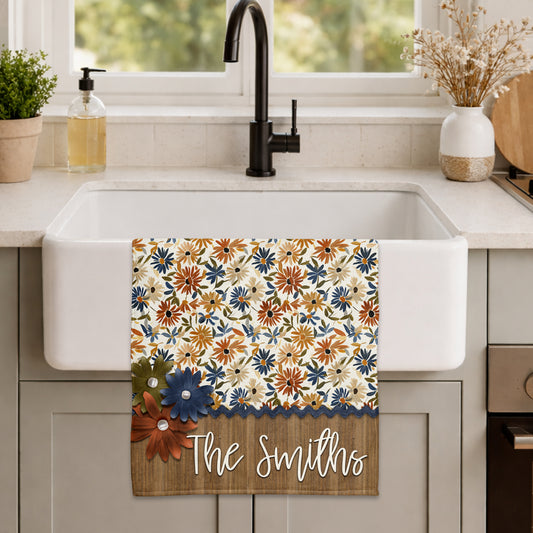 Personalized fall kitchen towel featuring navy, rust, golden yellow, and olive floral patterns with layered flower accents, navy trim, and a rustic wood-look family name panel.