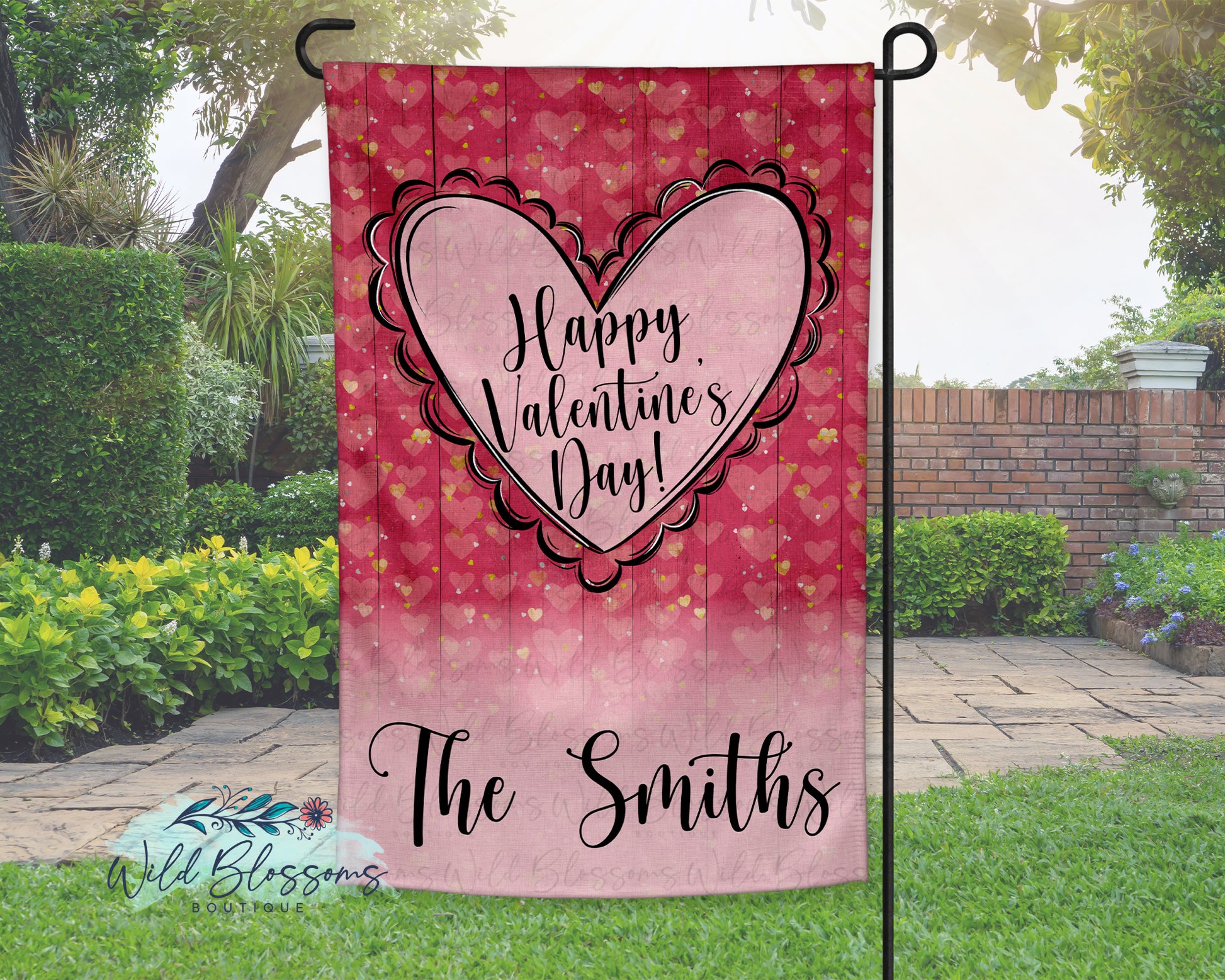 Valentine's Day-themed garden flag with heart design and 'Happy Valentine's Day!' text, displayed outdoors.