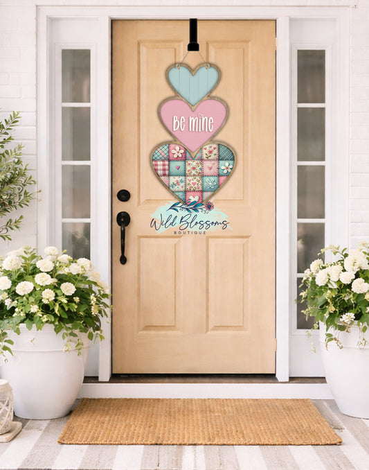 Decorative heart-shaped door hanger on a wooden door with flowers on either side.